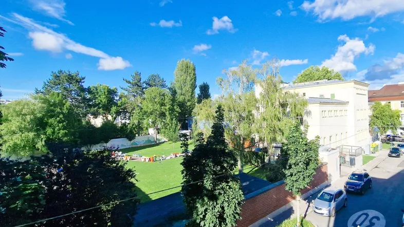 Weitläufiger Blick auf eine grüne Parkanlage mit Bäumen und blauem Himmel von einem Balkon aus.