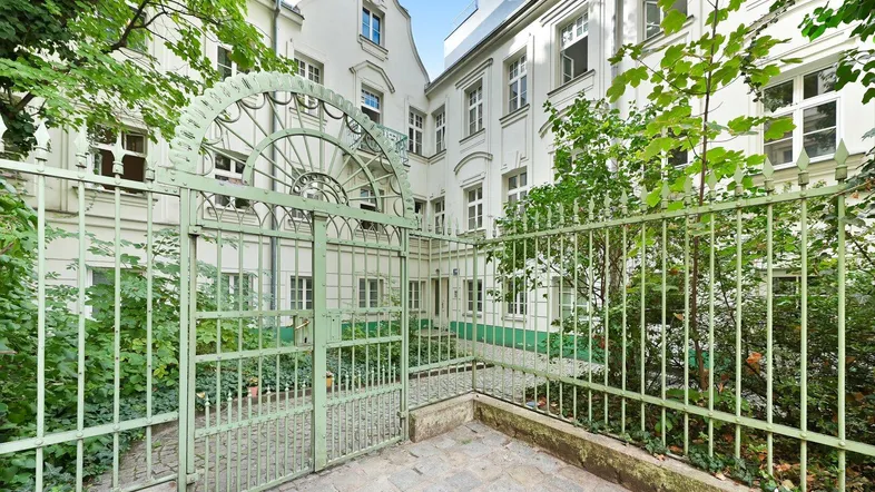 Innenhof mit schmiedeeisernem Tor und grünen Pflanzen, umgeben von historischen Gebäuden.