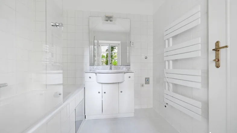 Helles Badezimmer mit weißen Fliesen, Badewanne, Waschtisch und beheiztem Handtuchhalter.