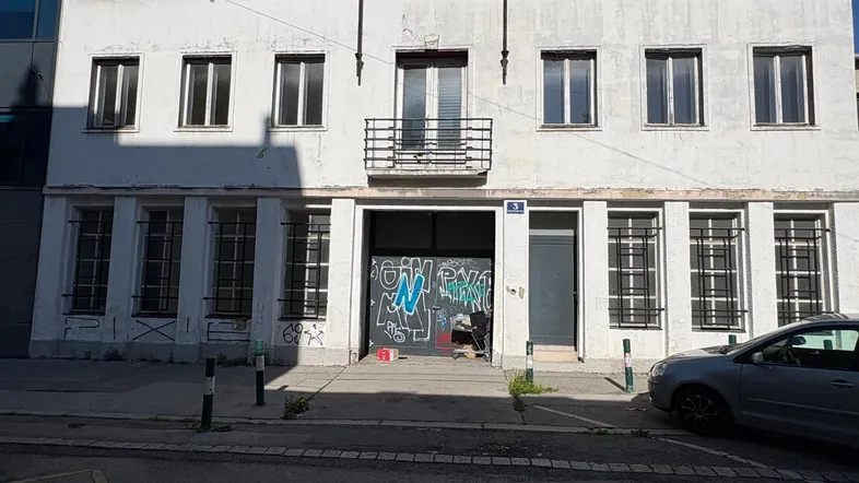 Fassade eines älteren Gebäudes mit mehreren Fenstern, einem kleinen Balkon und einem Eingang mit Graffiti.