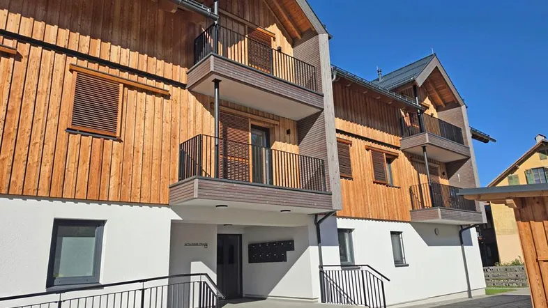 Modernes Gebäude mit Holzfassade, Balkonen und barrierefreiem Zugang zum Eingangsbereich.