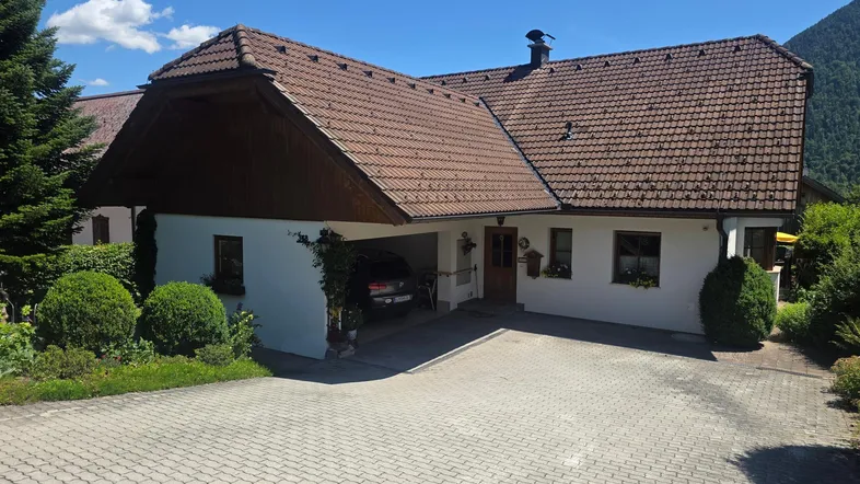 Traditionelles Haus mit Ziegeldach und integriertem Carport, umgeben von gepflegter Grünfläche.