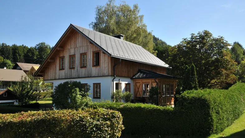 Traditionelles Haus mit Holzfassade und Satteldach, umgeben von einem gepflegten Garten und Hecken.