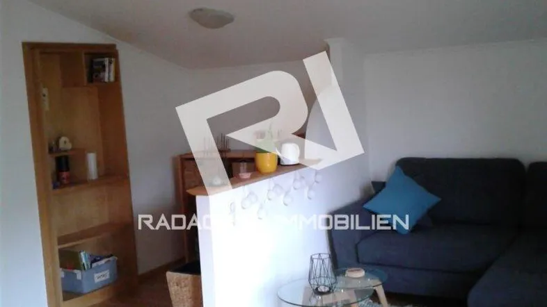 Helles Wohnzimmer mit Holzboden, Sofa und einem Regal, das den Raum optisch unterteilt.