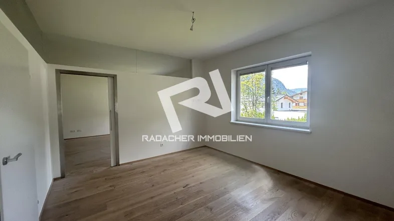 Helles, unmöbliertes Zimmer mit Holzboden und Blick ins Grüne, bereit für die individuelle Gestaltung.