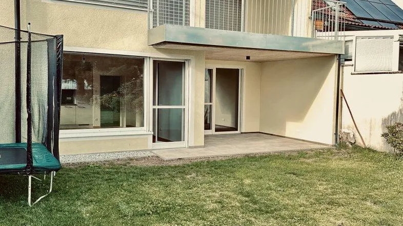 Moderne Hausfassade mit Terrasse, Rasenfläche und Balkon im Obergeschoss.