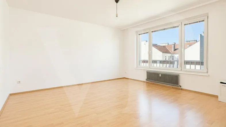 Helles Zimmer mit Parkettboden und großem Fenster, das viel Tageslicht hereinlässt.