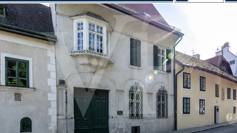 Historisches Gebäude mit traditioneller Fassade, Erkerfenster und grünen Fensterläden an einer Kopfsteinpflasterstraße.