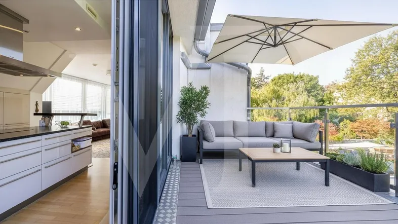 Geräumiger Balkon mit modernen Loungemöbeln, Sonnenschirm und Blick in die offene Küche.