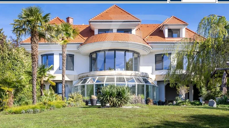 Großzügige Villa mit gepflegtem Vorgarten, Palmen und einem gläsernen Wintergarten.