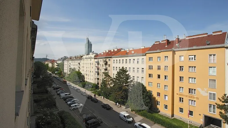 Blick von oben auf eine belebte Straße mit parkenden Autos und hohen Wohngebäuden.