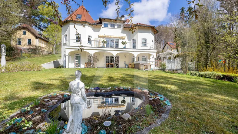 Großzügige Villa mit weitläufigem Garten, Teich und gepflegter Rasenfläche unter blauem Himmel.