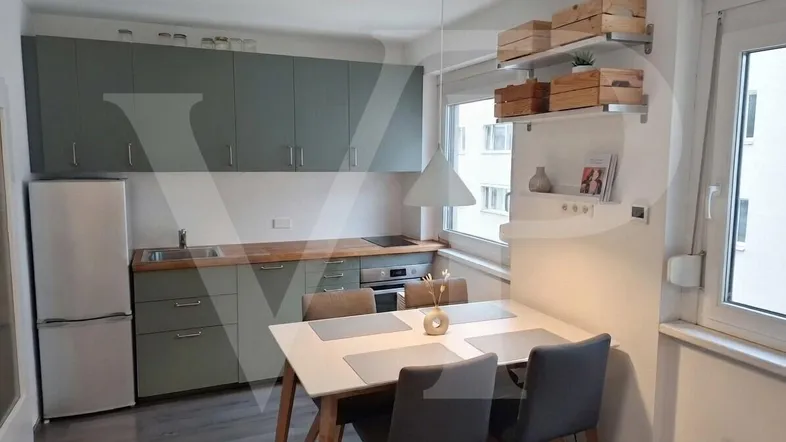Moderne Küche mit hellgrünen Schränken, Holzarbeitsplatte und Essbereich am Fenster.