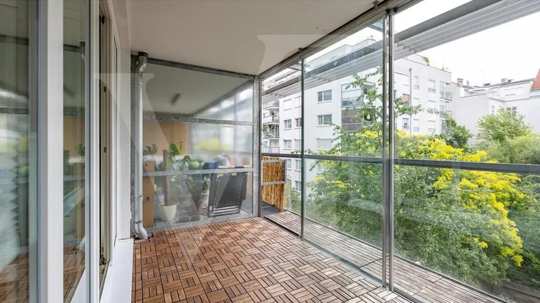 Verglaste Loggia mit Holzboden und Blick ins Grüne, ideal für entspannte Stunden im Freien.