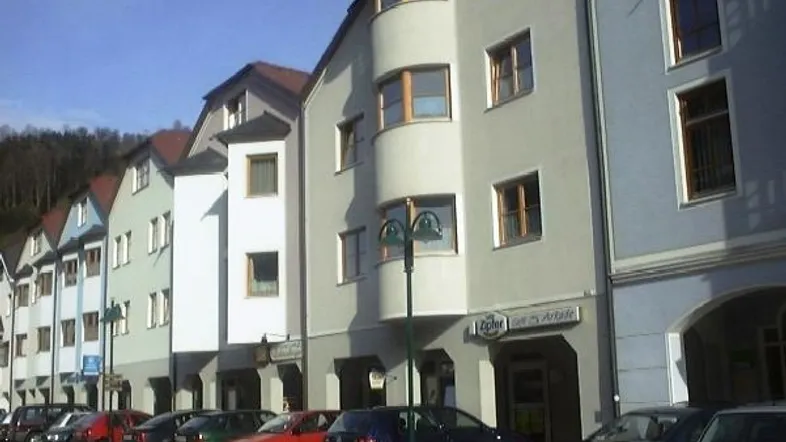 Reihe von Gebäuden mit moderner Architektur und geparkten Autos entlang einer Straße in einer städtischen Umgebung.