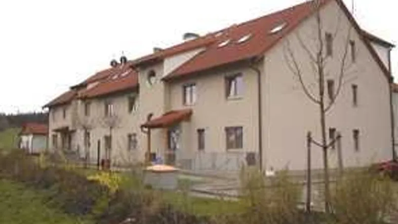 Reihenhäuser mit beiger Fassade und roten Ziegeldächern in einer grünen, ländlichen Umgebung.