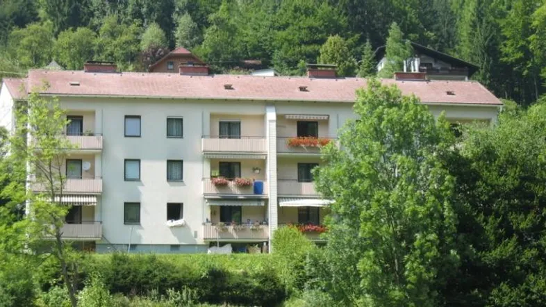 Mehrfamilienhaus mit mehreren Balkonen, umgeben von üppiger grüner Vegetation und Bäumen.