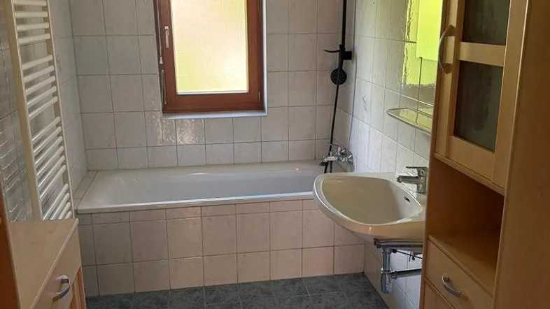 Helles Badezimmer mit Badewanne, Waschbecken, Fenster und Handtuchheizkörper.