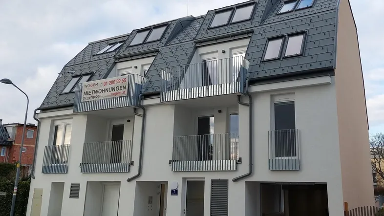 Neubau mit moderner Architektur, weißer Fassade, Satteldach und mehreren Balkonen.