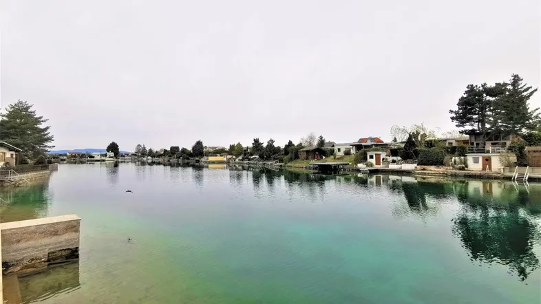 Blick auf den ruhigen Kanal mit Häusern am Ufer unter einem bewölkten Himmel.