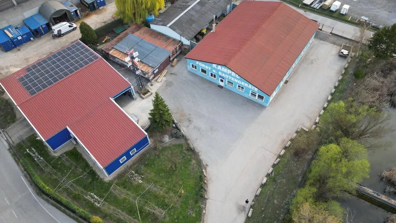 Luftaufnahme des Gewerbegebiets mit mehreren Gebäuden, darunter eines mit Solaranlage auf dem Dach und weiten Freiflächen.