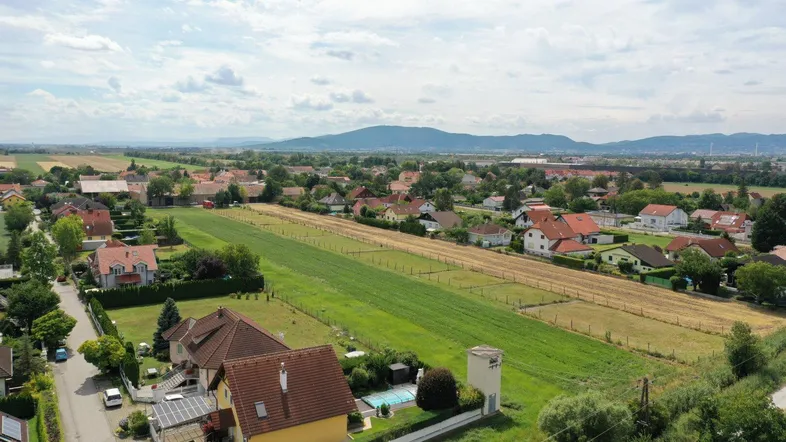Luftaufnahme einer ländlichen Wohnsiedlung mit Feldern, einem Pool und Bergen im Hintergrund.