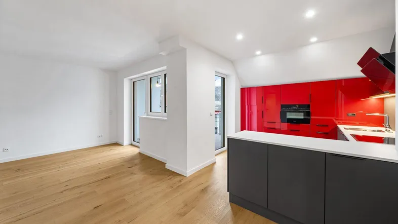 Heller offener Wohnbereich mit moderner roter Küche, Holzboden und Zugang zu einem Balkon.