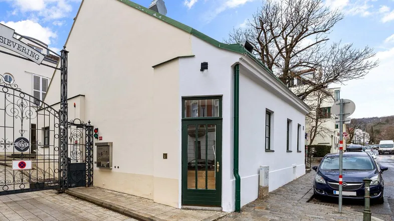 Weißes Gebäude mit grünen Akzenten und Eingangstür an einer gepflasterten Straße.