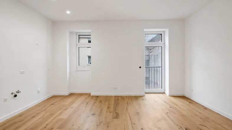 Geräumiges, unmöbliertes Zimmer mit hellem Holzboden und großen Fenstern.