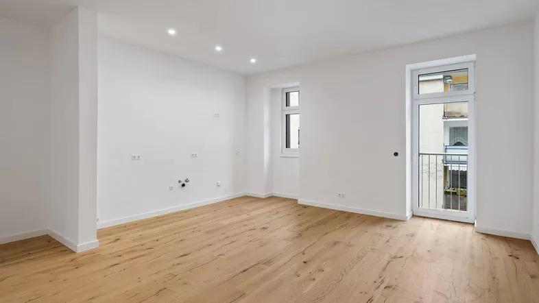 Helles, leeres Zimmer mit neuem Holzboden und Zugang zu einem französischen Balkon.