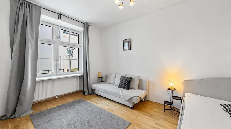 Helles Schlafzimmer mit Parkettboden, großem Fenster und gemütlichem Sofa.