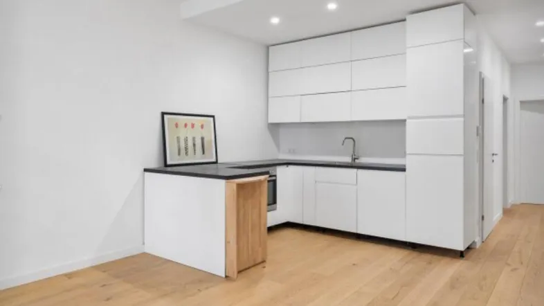 Moderne Einbauküche mit weißen Schränken, dunkler Arbeitsplatte und hellem Holzfußboden.
