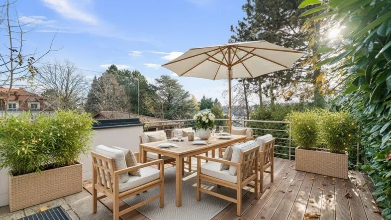 Möblierte Holzterrasse mit Sonnenschirm, Esstisch und Pflanzen in Töpfen.