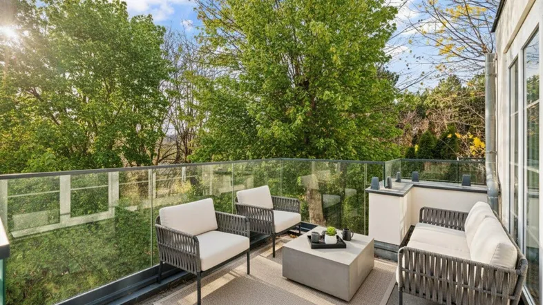Möblierte Terrasse mit Glasgeländer und Blick auf Bäume, ideal für entspannte Stunden im Freien.