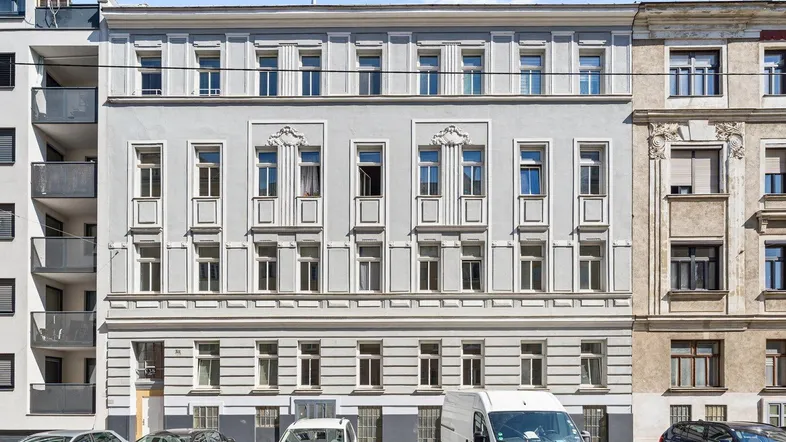 Historische Fassade eines Mehrfamilienhauses mit klassischer Architektur und vielen Fenstern.
