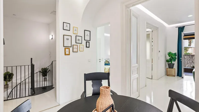 Heller Essbereich mit schwarzem Esstisch, gerahmten Bildern an der Wand und Zugang zu einer Treppe.