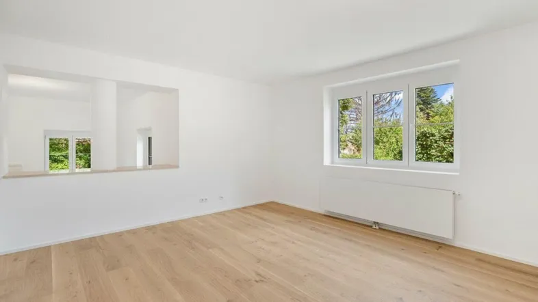 Helles Zimmer mit Holzboden und Blick ins Grüne, ideal als Wohn- oder Schlafbereich.
