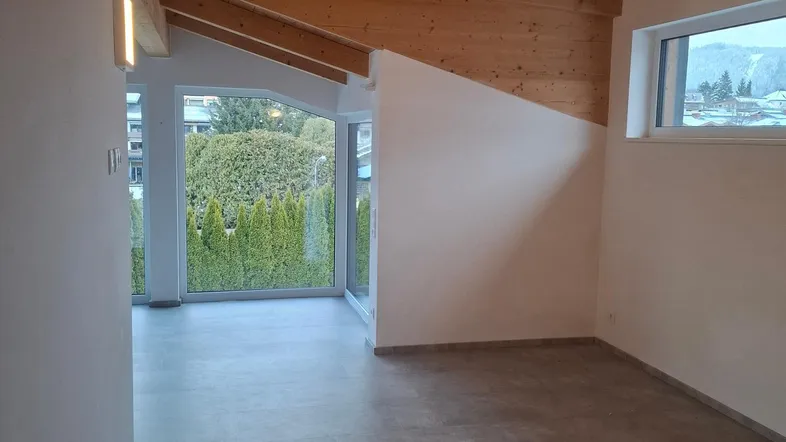 Heller Innenraum mit sichtbaren Holzbalken, großen Fenstern und Blick ins Grüne.