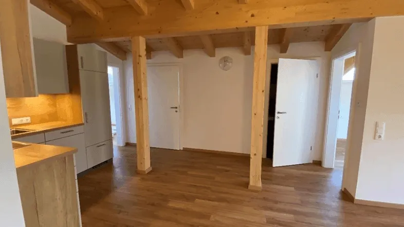 Heller offener Wohn- und Essbereich mit Holzbalkendecke und integrierter Küchenzeile.