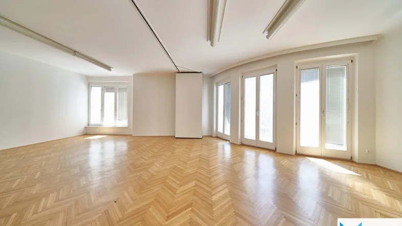 Geräumiger, heller Raum mit Fischgrätparkett und großen Fenstern, ideal für Büro oder Wohnen.