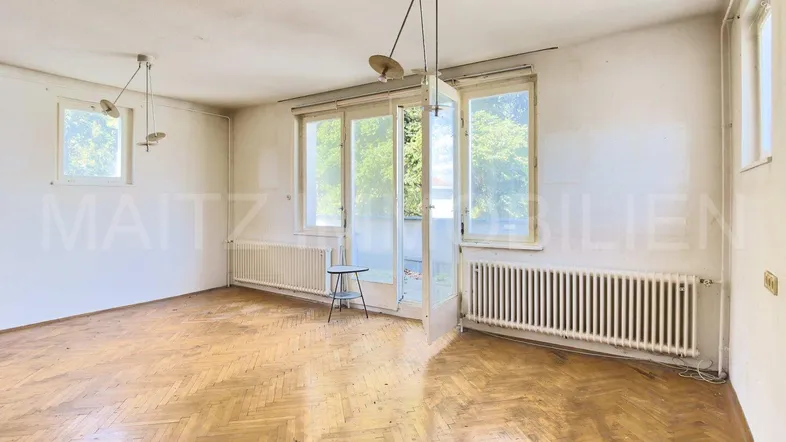 Helles Wohnzimmer mit Fischgrätparkett, weißen Wänden und Zugang zu einem Außenbereich.