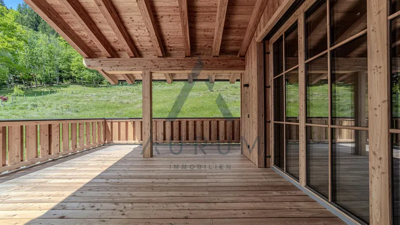 Geräumige Holzterrasse mit Blick auf die grüne Landschaft und großen Glasfronten.
