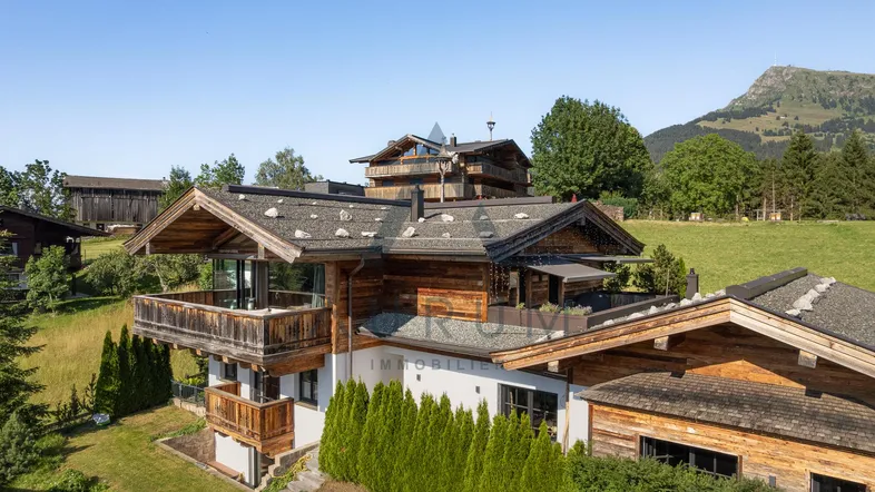 Traditionelles Chalet mit Holzbalkonen und Bergblick in grüner Umgebung.