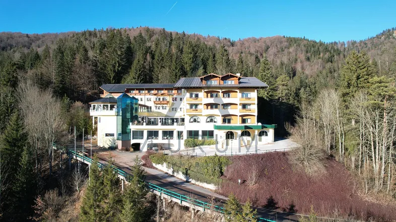 Großes Hotelgebäude in den Bergen, umgeben von Wald, mit sonnigem Wetter und moderner Architektur.