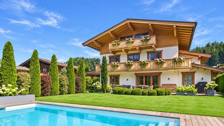 Großzügiger Gartenbereich mit privatem Pool und traditionellem Alpenhaus unter blauem Himmel.