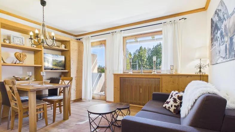 Gemütlicher Wohn-Essbereich mit Holzelementen, Esstisch und Blick ins Grüne durch große Fenster.