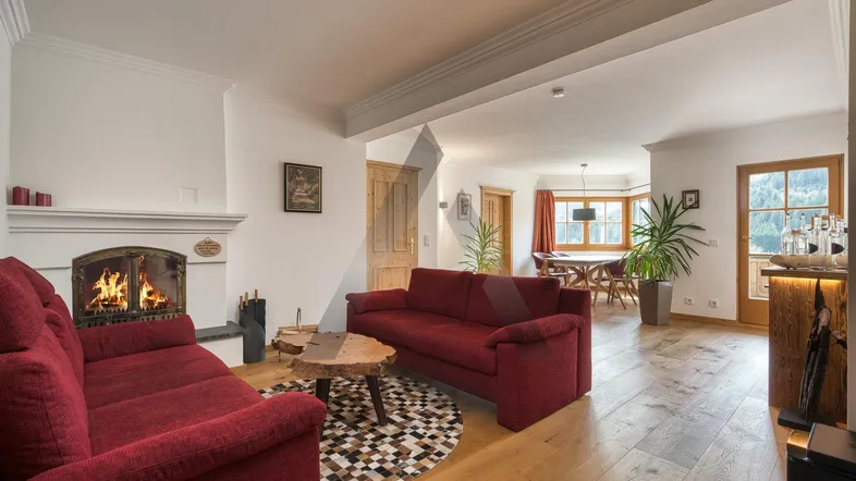 Gemütlicher Wohn-Essbereich mit Kamin, Holzboden und roten Sofas, ideal für entspannte Abende.