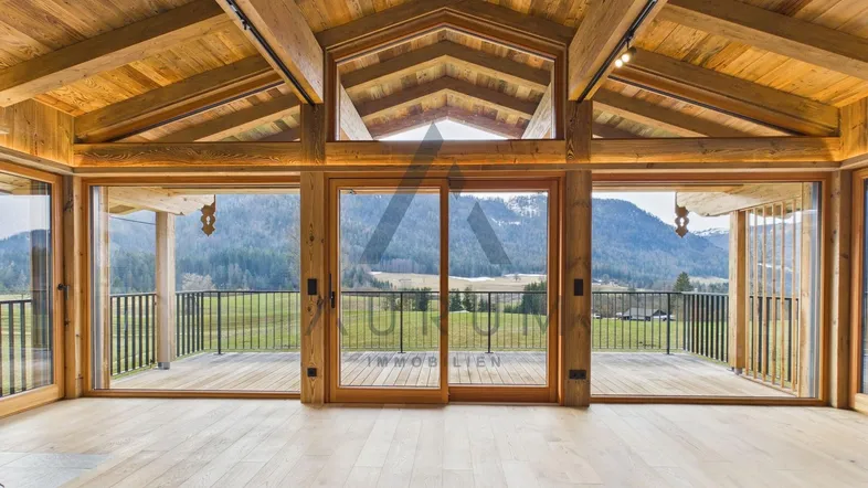 Geräumiger Wohnbereich mit hohen Holzdecken, großen Glasfronten und weitem Blick auf die Berge.