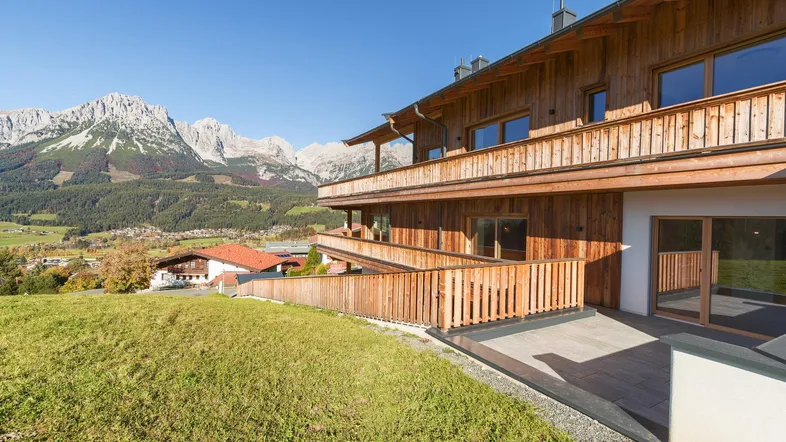 Modernes Holzgebäude mit mehreren Balkonen und Terrassen in einer malerischen Berglandschaft.