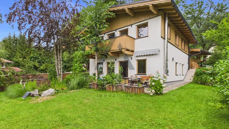 Hausfassade mit gepflegtem Garten, Rasenfläche und kleinen Blumenbeeten.